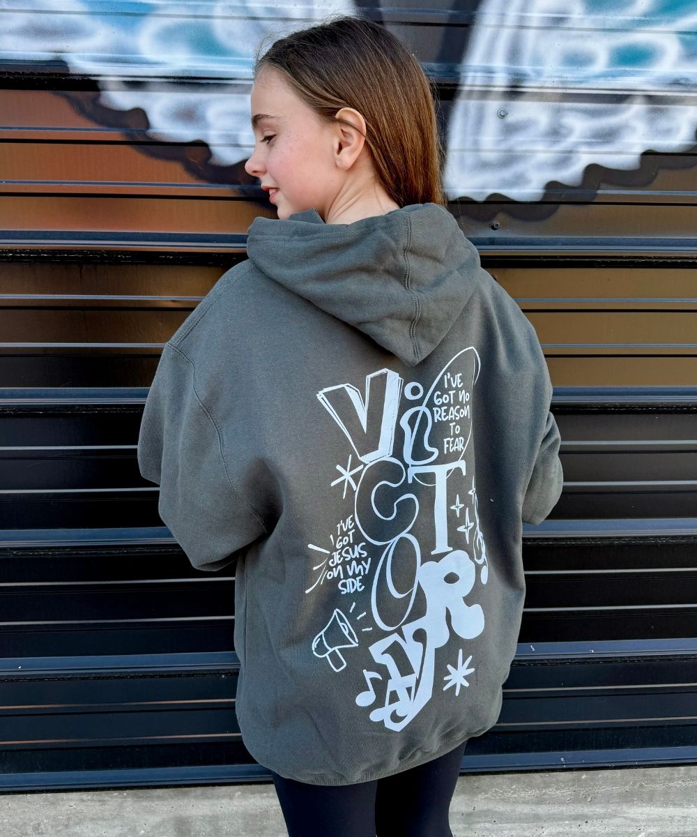 Person wearing a gray hoodie with white text and graphics on the back, standing in front of a graffiti-covered wall.
