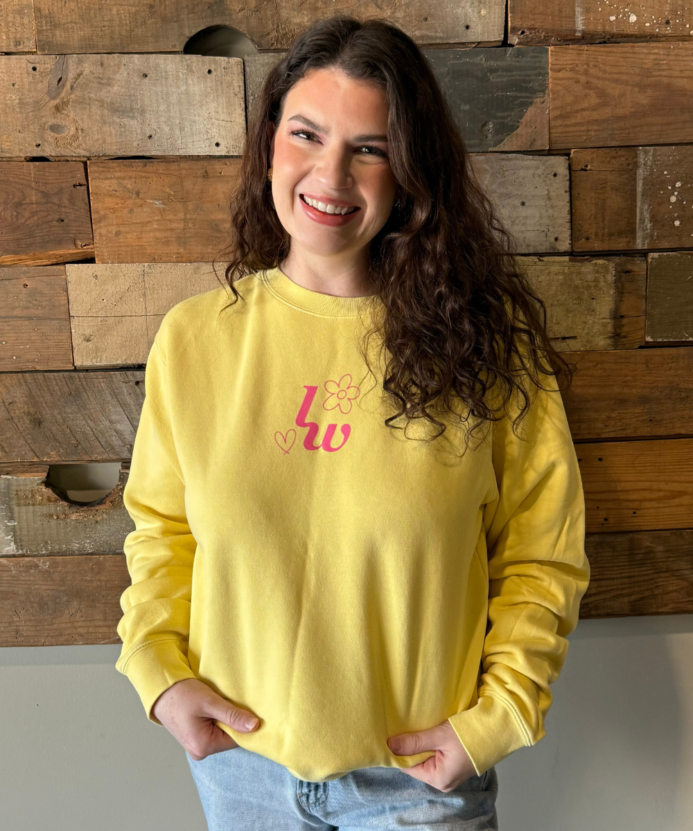 Person wearing a yellow sweatshirt with a design in front of a wooden wall.