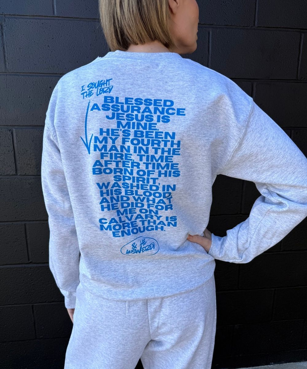 Person wearing a light gray sweatshirt with blue text against a dark brick wall.