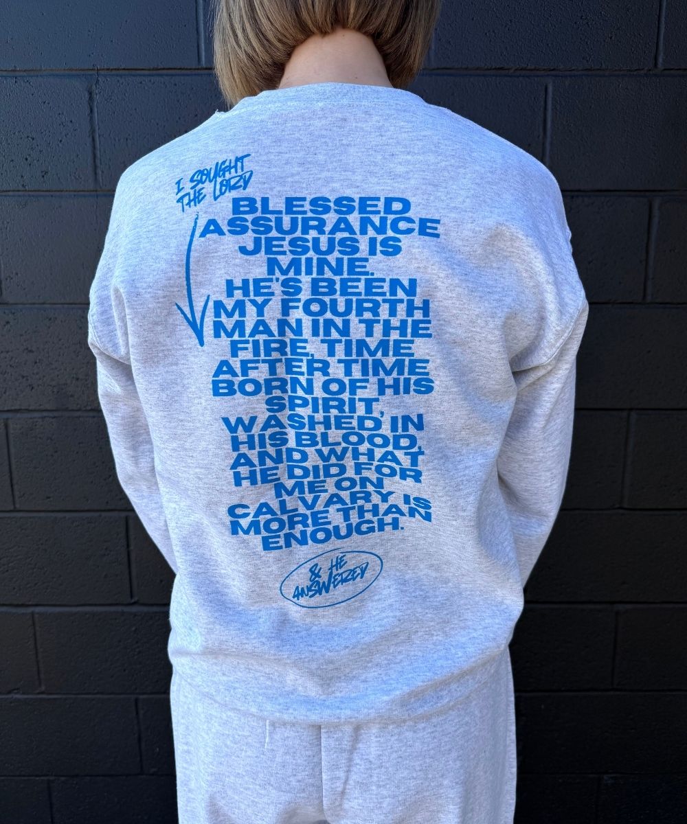 Person wearing a light blue sweatshirt with text on the back against a dark brick wall.