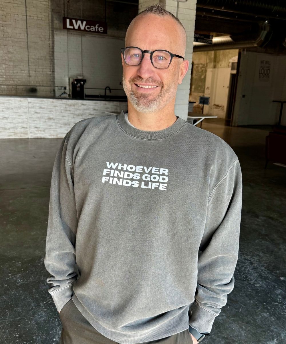 Man wearing a gray sweatshirt with text in an indoor setting