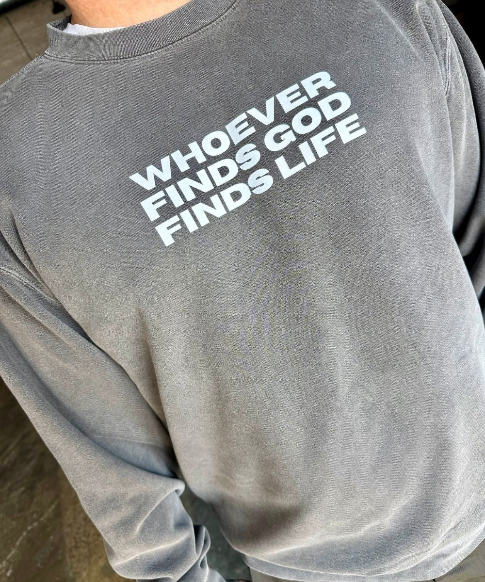 Gray sweatshirt with text 'WHOEVER FINDS GOD FINDS LIFE' on a person wearing it.