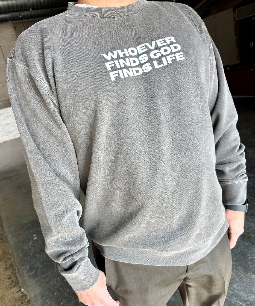 Gray sweatshirt with text 'WHOEVER FINDS GOD FINDS LIFE' on the back, worn by a person.