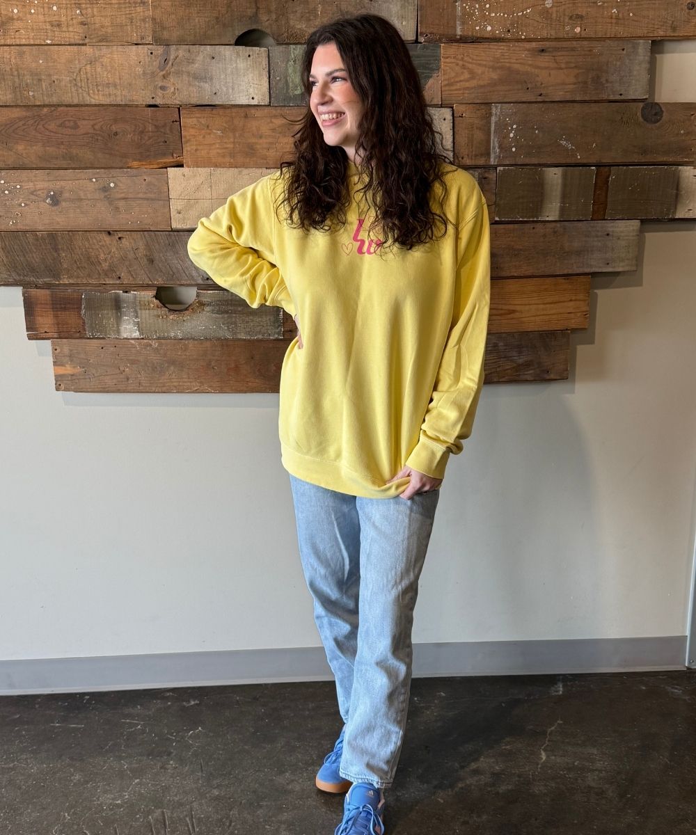 Person wearing a yellow sweatshirt with a graphic design, standing against a wooden wall.