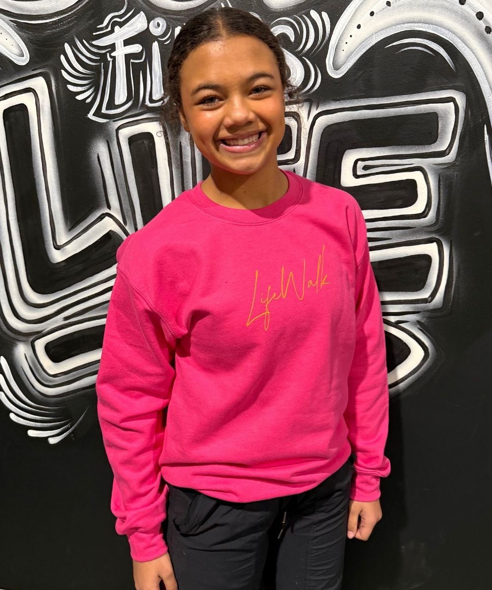 Person wearing a pink sweatshirt with 'Life Walk' text in front of a black and white patterned wall.