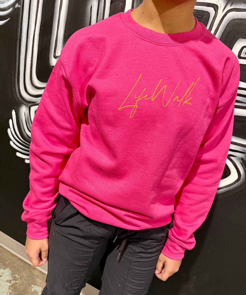 Person wearing a bright pink sweatshirt with 'Life Walk' text against a black and white patterned background