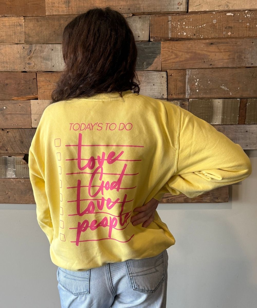Person wearing a yellow sweatshirt with a motivational quote on the back, standing against a wooden paneled wall.