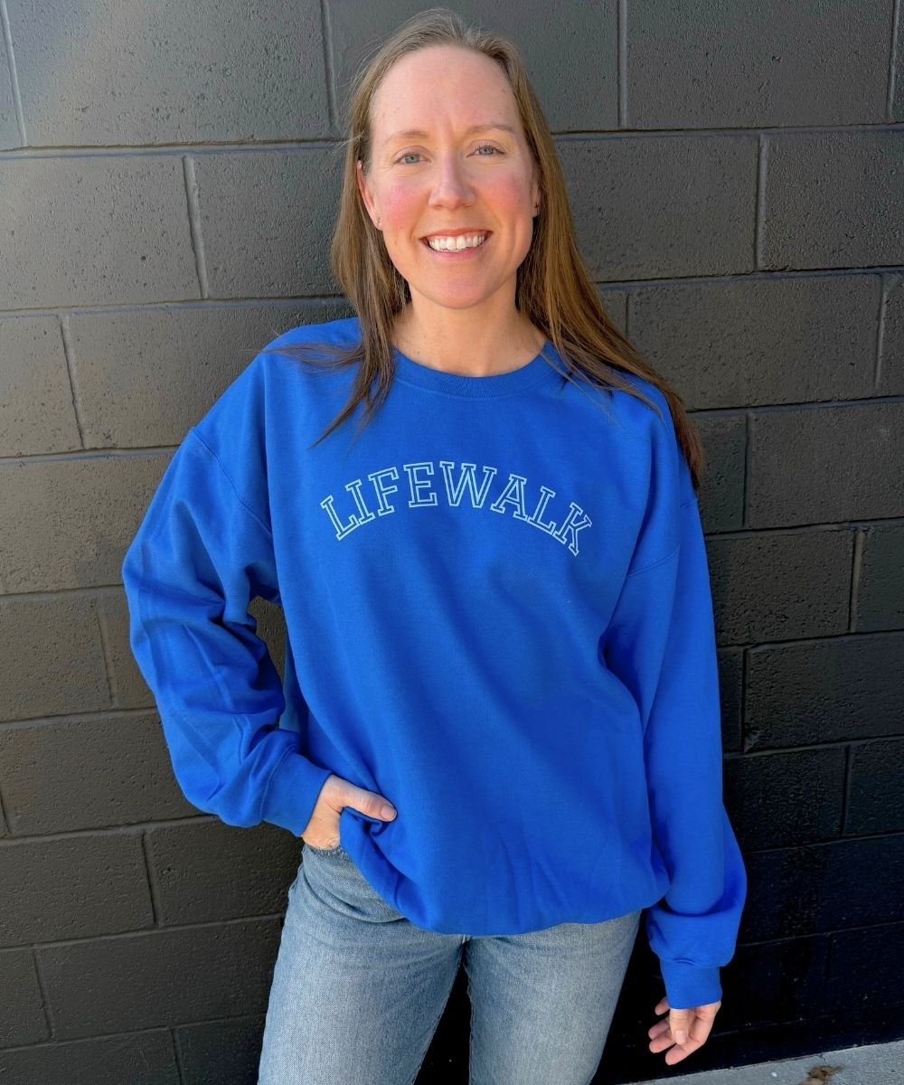 Woman wearing a blue sweatshirt with 'LIFEWALK' text against a brick wall.