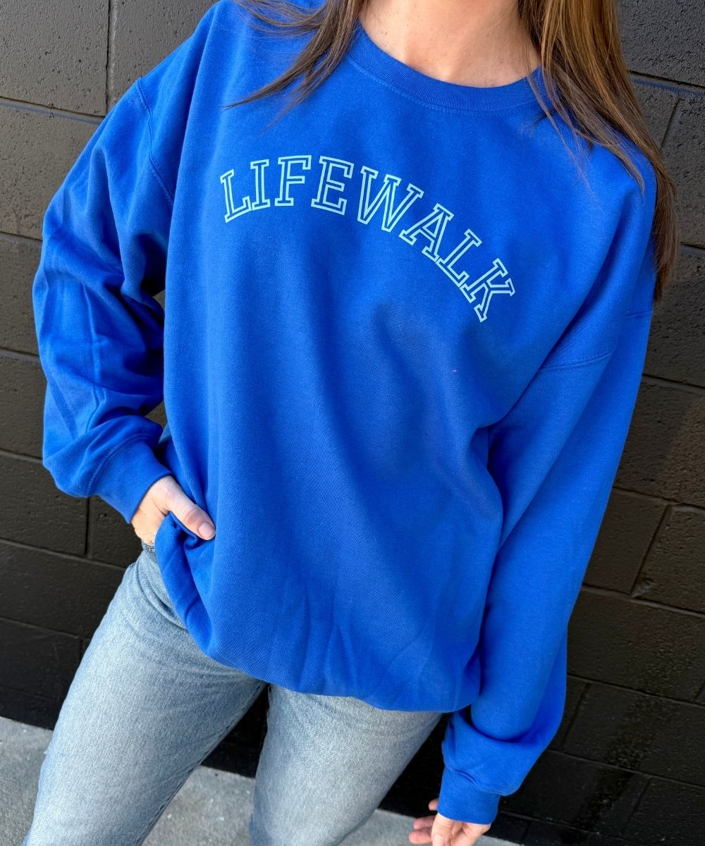 Person wearing a blue sweatshirt with 'LIFEWALK' text against a brick wall.