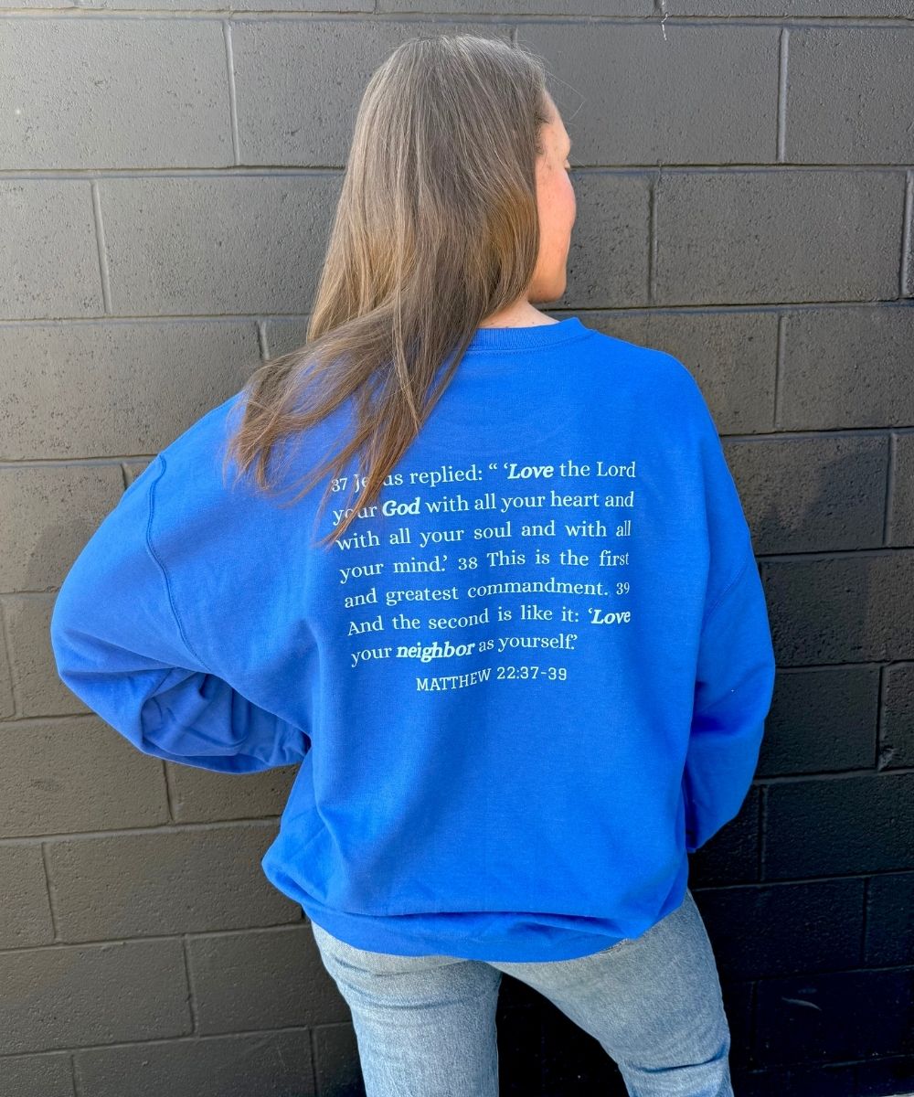 Person wearing a blue sweatshirt with text on the back, standing against a brick wall.