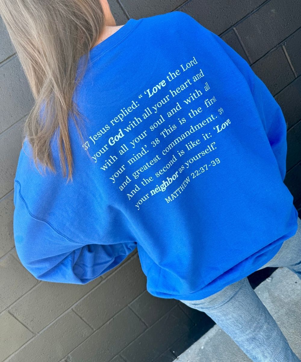 Person wearing a blue sweatshirt with text on the back, standing against a tiled wall.